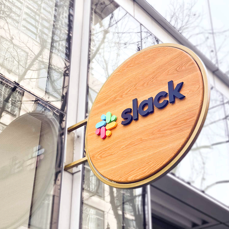 Wood blade sign with dimensional color logo and brass hardware for the San Francisco brand space at Slack, an American cloud-based set of team collaboration tools and services.