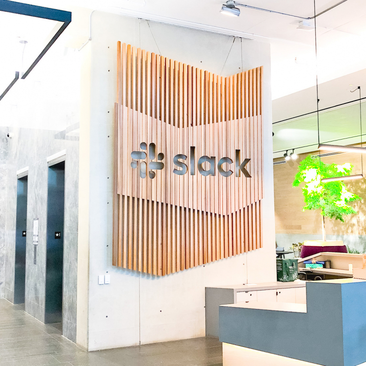 Modern, large-scale slat wood lobby sign on concrete wall at the San Francisco lobby of Slack, an American cloud-based set of team collaboration tools and services.